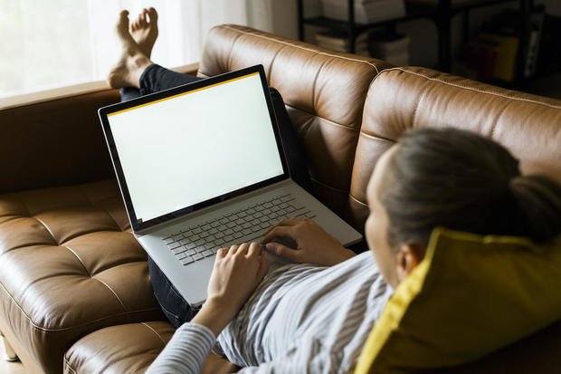 Jovem deitada no sofá em casa usando laptop 